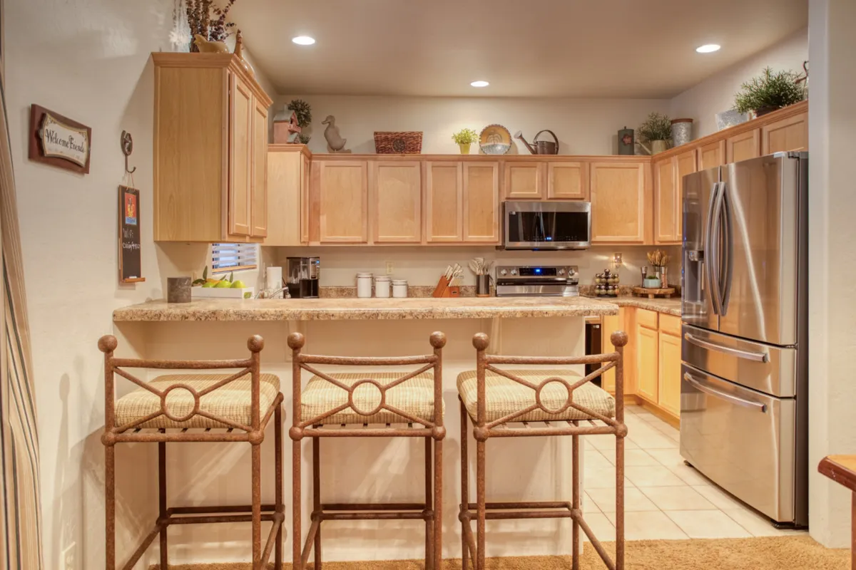 A warm, communal kitchen space featuring a central island with stools, sleek stainless steel appliances, and rich wood cabinetry. The setup encourages both meal prep and casual gatherings, with plenty of room for group activities like baking or sharing morning coffee.