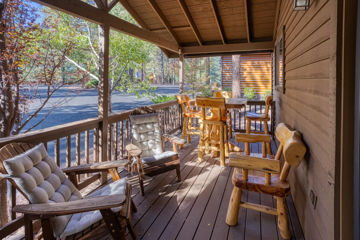 This image highlights a welcoming outdoor deck scene furnished with wooden chairs and a table, surrounded by lush greenery and tall pines. The setting captures both the tranquility of sunrise and the warmth of evening gatherings, illustrating the ongoing connection to nature and the versatility of the outdoor space.