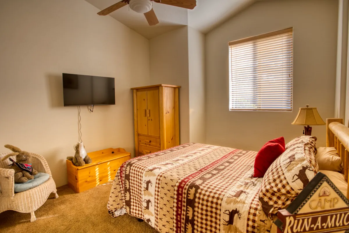 A view of a versatile bedroom or loft area featuring a bed, ceiling fan, TV, dresser, and lamp. The setting is both functional and welcoming, suggesting a space suitable for families or friends to relax, watch television, or read together.