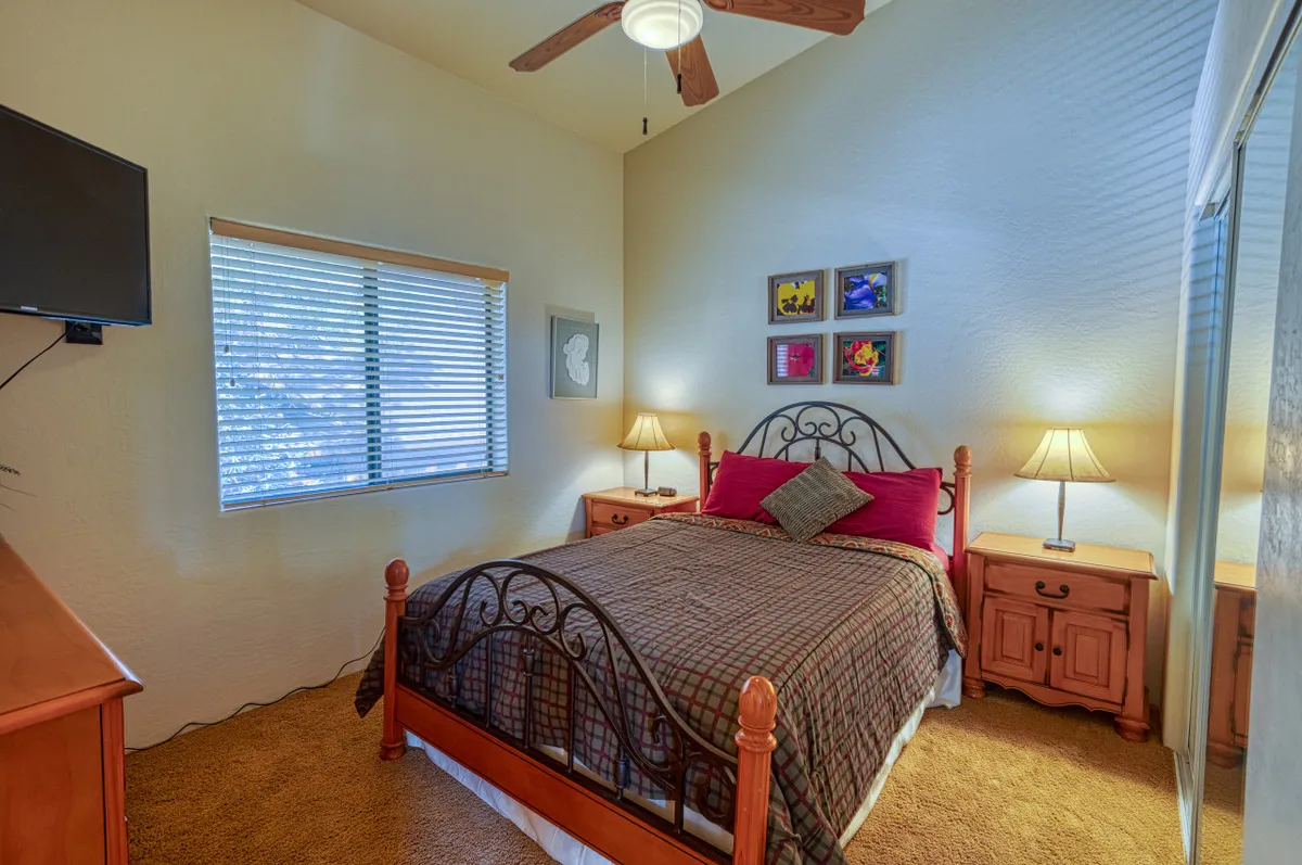 A cozy bedroom with a comfortable bed, nightstands, attractive artwork, and a large window that lets in plenty of daylight. The setting is peaceful and well-suited to restful sleep or quiet moments.