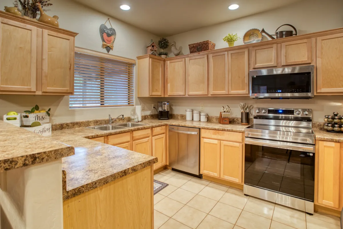 A modern kitchen highlighted by gleaming stainless steel appliances, granite countertops, and classic wooden cabinets. A window with blinds lets in natural light, creating an inviting atmosphere ideal for cooking and gathering.